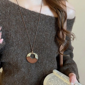 Detail of vintage geometric wood and gold pendant on model wearing dark sweater