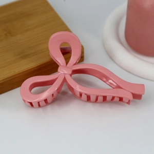 Detail of pink bow hair claw clip with glossy finish and dense teeth for secure styling
