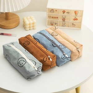 Corduroy smiley face pencil cases in four pastel colors on a white minimalist table