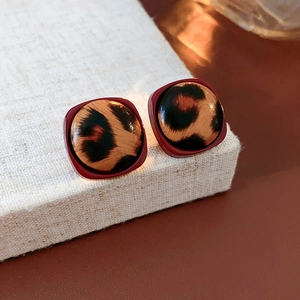 Detailed view of leopard print square acrylic earrings with deep red border on linen