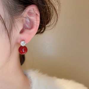 Macro detail of red pearl and zircon drop earring worn by a model in soft lighting