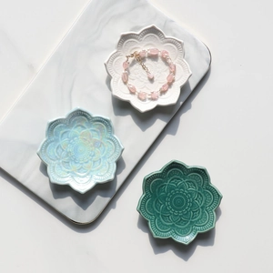 Three flower-shaped ceramic jewelry trays in white, blue, and green on marble surface