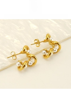 Close-up of C-shaped 18K gold plated earrings with white pearls on a textured background