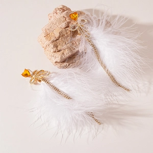 Detail of amber heart crystal and white feather tassel earrings on a textured stone base
