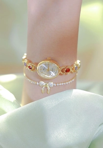 Detail of gold quartz watch with colorful gems and matching bow bracelet on silk