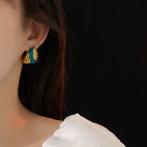 Macro detail of vintage gold textured metal and teal enamel triangle earring on model