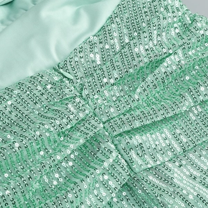 Detailed view of mint green sequins and smooth satin fabric on a backless evening dress