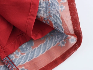 Detailed close-up of stitching and floral print lining on red chiffon shirt edge
