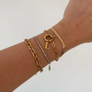 Detail of layered gold titanium steel bracelet set featuring an L-letter pendant and chains