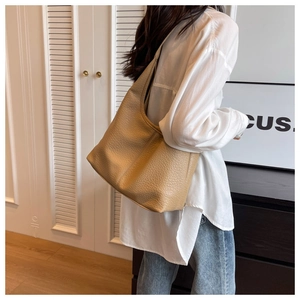 Detail shot of a khaki pebble leather tote bag worn by a model in a minimalist interior