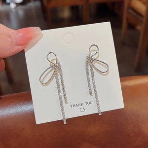Detail of silver bowknot earrings featuring long rhinestone tassels on display