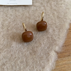 Macro shot of C-shaped square tiger eye stone earrings on a warm textured background