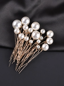 Detail of gold U-shaped hair pins with white pearls on a black silk background