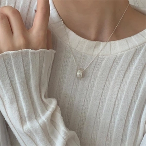 Detail of silver cylindrical zircon heart pendant necklace worn on a cream sweater