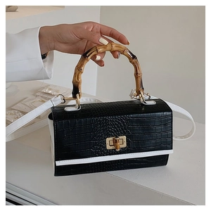 Close-up of black crocodile embossed leather handbag with bamboo handle and gold twist lock
