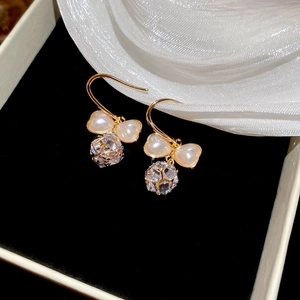 Detailed view of golden bow earrings with heart pearls and crystals on black velvet