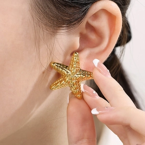 Close-up of golden hollow starfish earrings with textured surface on a model's ear