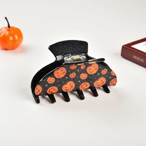 Detail of a large black glitter Halloween hair claw clip with orange pumpkin patterns