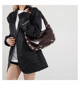 Close-up of a dark brown crescent bag with silver studs on a model wearing black