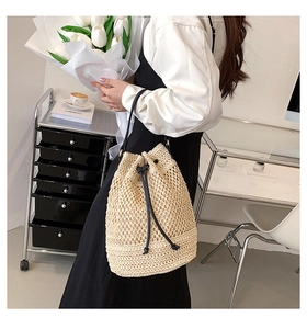 Chic beige woven straw bucket bag with black drawstrings worn by a model in casual setting