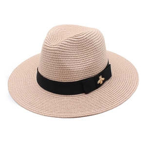 Detailed macro view of beige straw hat featuring black ribbon and gold bee accent