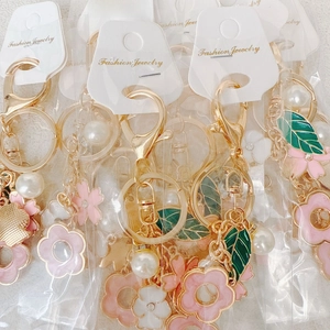 Detailed view of enamel flower keychains with pearls and gold links on fashion display cards
