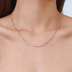Minimalist stainless steel necklace featuring gold beads on silver chain worn by model