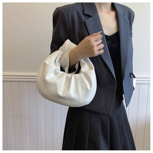 Detailed view of white minimalist dumpling bag with pleated texture held by a model