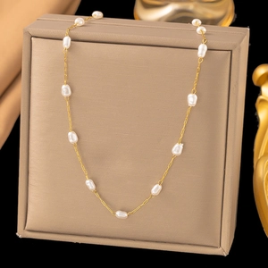 Detail of a golden chain necklace with baroque pearls on a beige jewelry display box