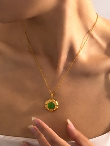 Detailweergave van een gouden titanium stalen ketting met ronde groene edelsteen hanger