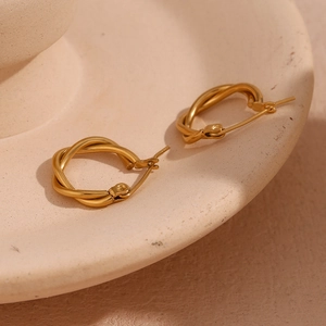 Detailed close-up of 18K gold plated stainless steel twisted hoop earrings on a beige tray