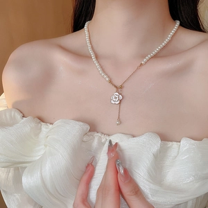 Close-up detail of white enamel camellia pearl necklace with gold chain and fringe