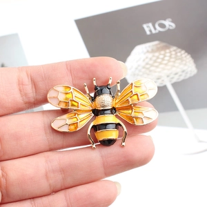 Macro shot of bee brooch with yellow enamel and translucent wings held by hand