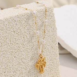 Detailed view of 18K gold plated coconut tree pendant and pearls on a stone backdrop