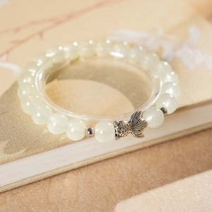Macro view of beaded bracelet with light green chalcedony and silver fish charm detail