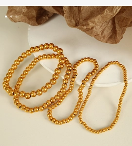 Macro view of golden stainless steel beaded bracelets in multiple sizes on textured background