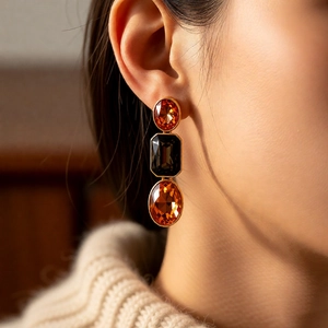 Close-up of vintage gold earrings with orange and black gems worn by a model