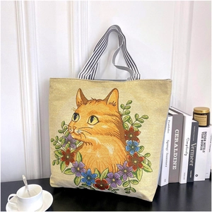 Detail of beige canvas tote bag with orange cat and flower embroidery on black table