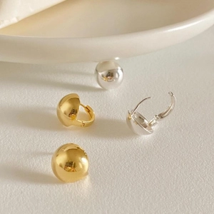 Detailed close-up of polished gold and silver spherical stud earrings on a ceramic tray