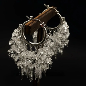 Silver hoop earrings with crystal tassels and star charms on a black display stand