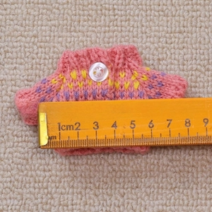 Detailed view of pink knitted doll sweater with colorful collar and scale measurement
