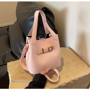 Detail of light pink pebbled leather bucket bag with metal buckle on stone pedestal