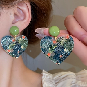 Close-up of heart-shaped tropical earrings featuring green palm leaf patterns and beads