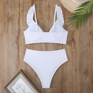 Flat lay of white ribbed bikini with ruffle straps and high waist bottom on wood background