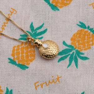 Macro view of gold necklace with oval pendant featuring white inlay and embossed texture