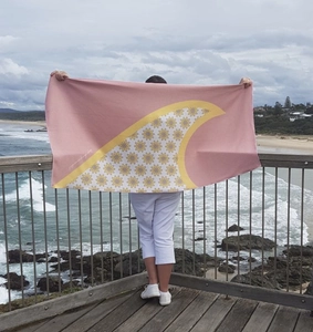 Pink quick-dry beach towel with yellow floral and fin pattern shown at the beach