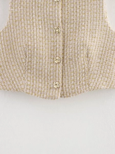 Detailed macro view of the tweed vest hem featuring elegant gold knot buttons and texture