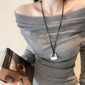 Dettaglio della collana con ciondolo a borsa argentata su cordino nero e maglione grigio