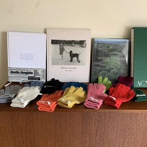 Multiple colorful knit touchscreen gloves arranged on a wooden surface with lifestyle books