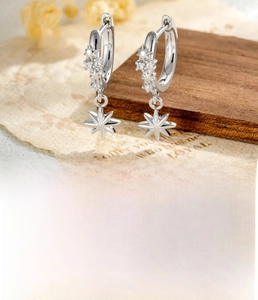 Macro detail of silver star pendant earrings with zircons and copper hoop design